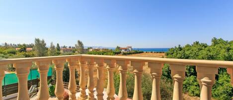 A balcony with a balustrade overlooking a landscaped area and a view of the sea.