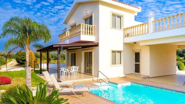 A two-story house with a swimming pool, a covered patio, and a garden with palm trees.