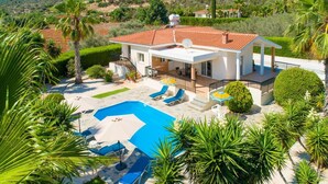 Ein modernes Haus mit Swimmingpool, umgeben von üppiger Vegetation und einer hügeligen Landschaft.