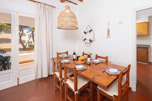 Un comedor con una mesa de madera, sillas, una lámpara colgante y vistas a través de un ventanal.