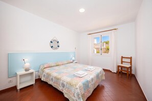 Une chambre à coucher comprenant un lit, des tables de chevet, une chaise, une fenêtre et un élément décoratif mural.