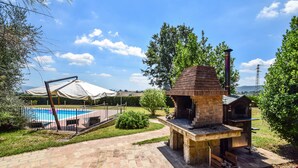 Ein Garten mit einem gemauerten Grill, einem Schwimmbecken und einer überdachten Terrasse.