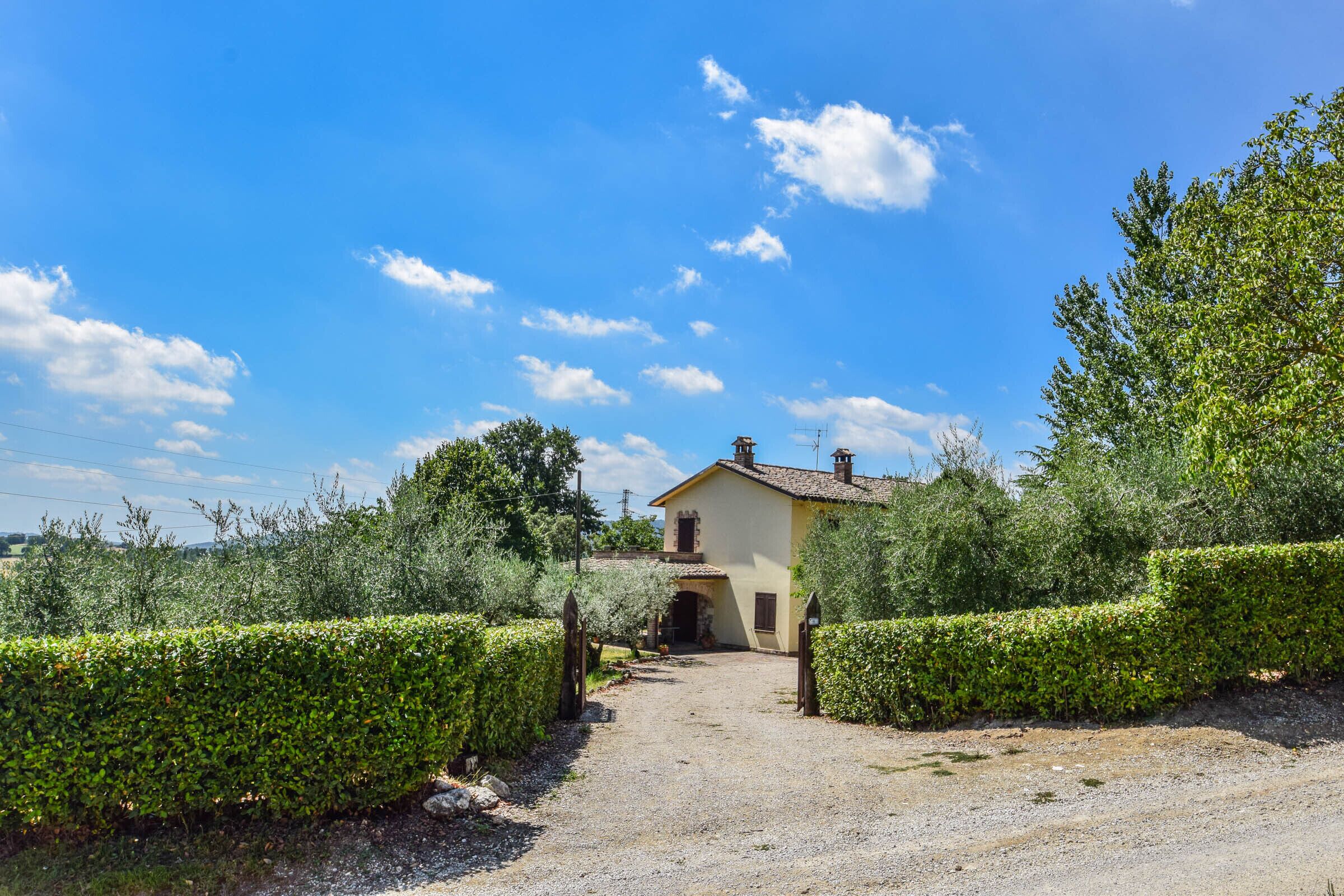 A rural house with a gravel driveway leading to a wooden gate.