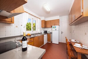 Eine kleine Küche mit Holzschränken, einem weißen Kühlschrank, einem Esstisch für vier Personen und einem Fenster mit Vorhängen.