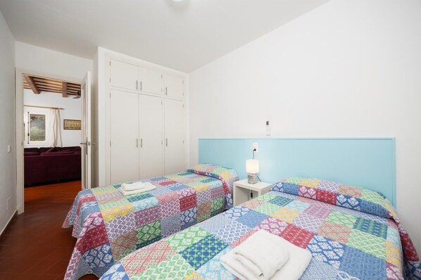 Un dormitorio con dos camas, un armario, una mesita de noche con lámpara y una ventana con cortinas.