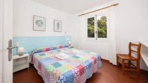 Ein Schlafzimmer mit einem Bett, einem Sessel, einem Nachttisch, einem Fenster und zwei gerahmten Bildern an der Wand.