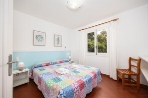 Ein Schlafzimmer mit einem Bett, einem Sessel, einem Nachttisch, einem Fenster und zwei gerahmten Bildern an der Wand.