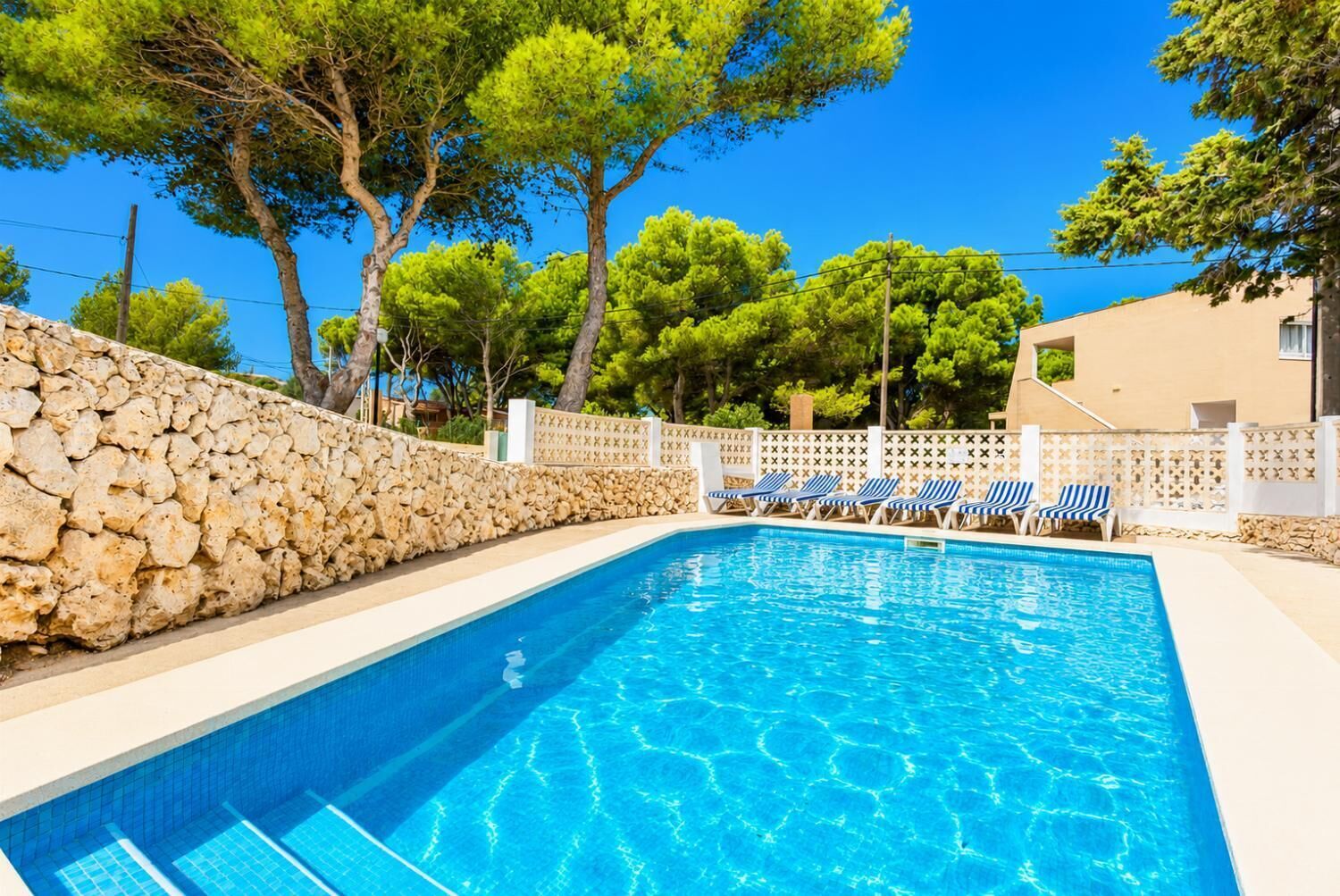 A swimming pool with lounge chairs and a stone wall.