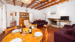 Ein Wohnzimmer mit Kamin, Fernseher, Esstisch für zwei Personen und Bücherregal.