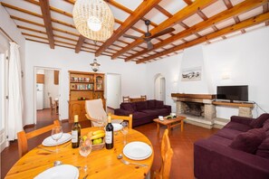 Ein Wohnzimmer mit Kamin, Fernseher, Esstisch für zwei Personen und Bücherregal.