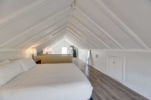 A spacious attic bedroom with a large bed, wooden flooring, and a sloped ceiling.