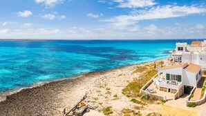 Une propriété située sur la côte, avec une plage, une eau d’un bleu limpide et des bâtiments blancs aux toits rouges.