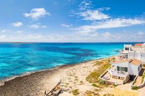 Une propriété située sur la côte, avec une plage, une eau d’un bleu limpide et des bâtiments blancs aux toits rouges.