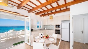 Une cuisine moderne avec des poutres en bois, un coin repas avec des chaises blanches et une vue sur la mer.