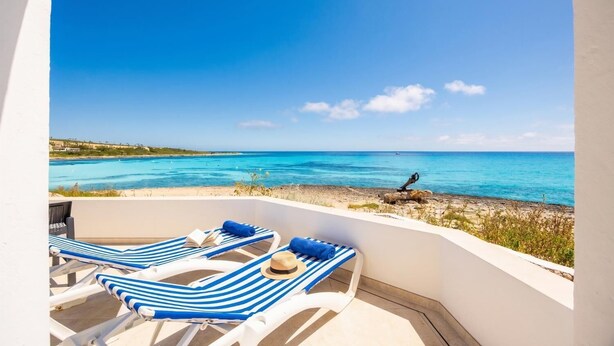 Un balcon avec deux fauteuils de jardin à rayures, un chapeau et une vue sur la mer et le littoral au loin.