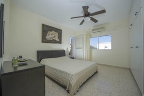 Une chambre à coucher avec un lit, un bureau, un ventilateur de plafond, une fenêtre et une porte.
