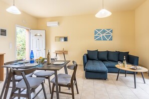 Ein Wohnzimmer mit einer Couch, einem Esstisch mit Stühlen und einem kleinen runden Tisch mit einer Flasche und Gläsern.