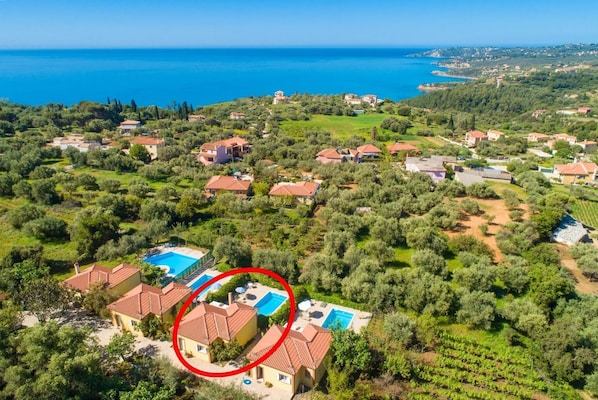 An aerial view of a coastal residential area with houses, olive groves, and a clear blue sea. - Villa Russa Anna - One Bedroom Villa, Sleeps 2 (Afrato)
