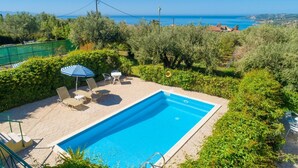 Piscina rectangular con sillas de descanso y una sombrilla, rodeada de vegetación y con vistas a un paisaje costero.