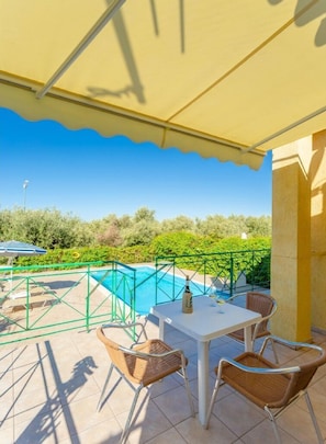 A covered outdoor area with a pool, a table with chairs, and a bottle of champagne.