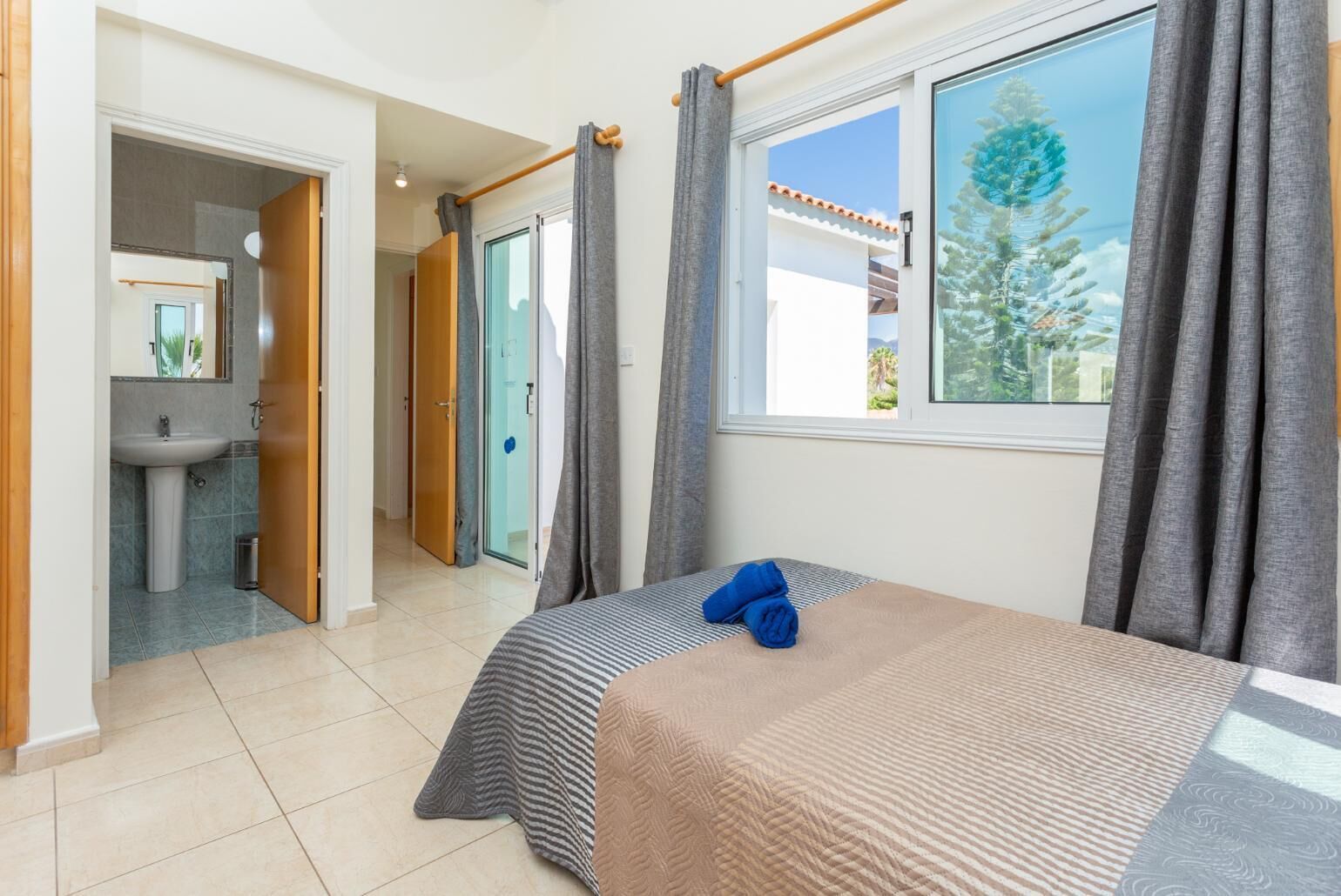 Une chambre à coucher avec un lit, une fenêtre avec des rideaux, une salle de bain avec un lavabo et une porte donnant sur une autre pièce.