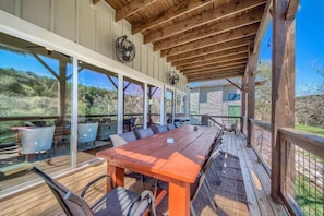 Une terrasse extérieure avec une table et des chaises en bois, entourée de murs en verre et de poutres en bois.