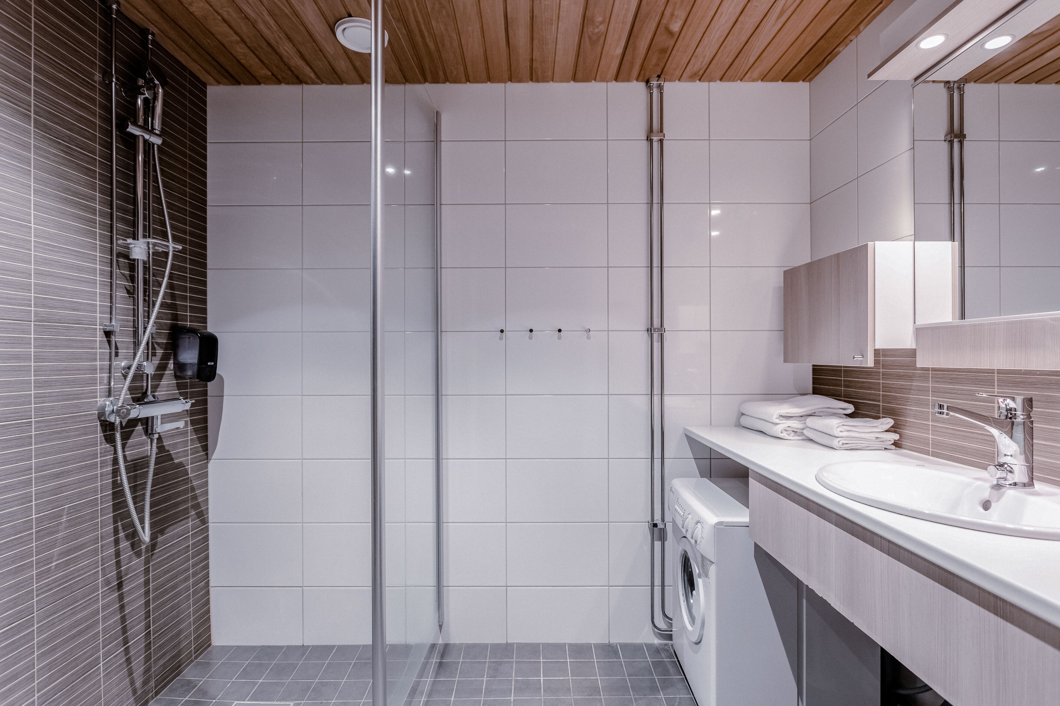 A modern bathroom with a shower, a sink, and a washing machine.