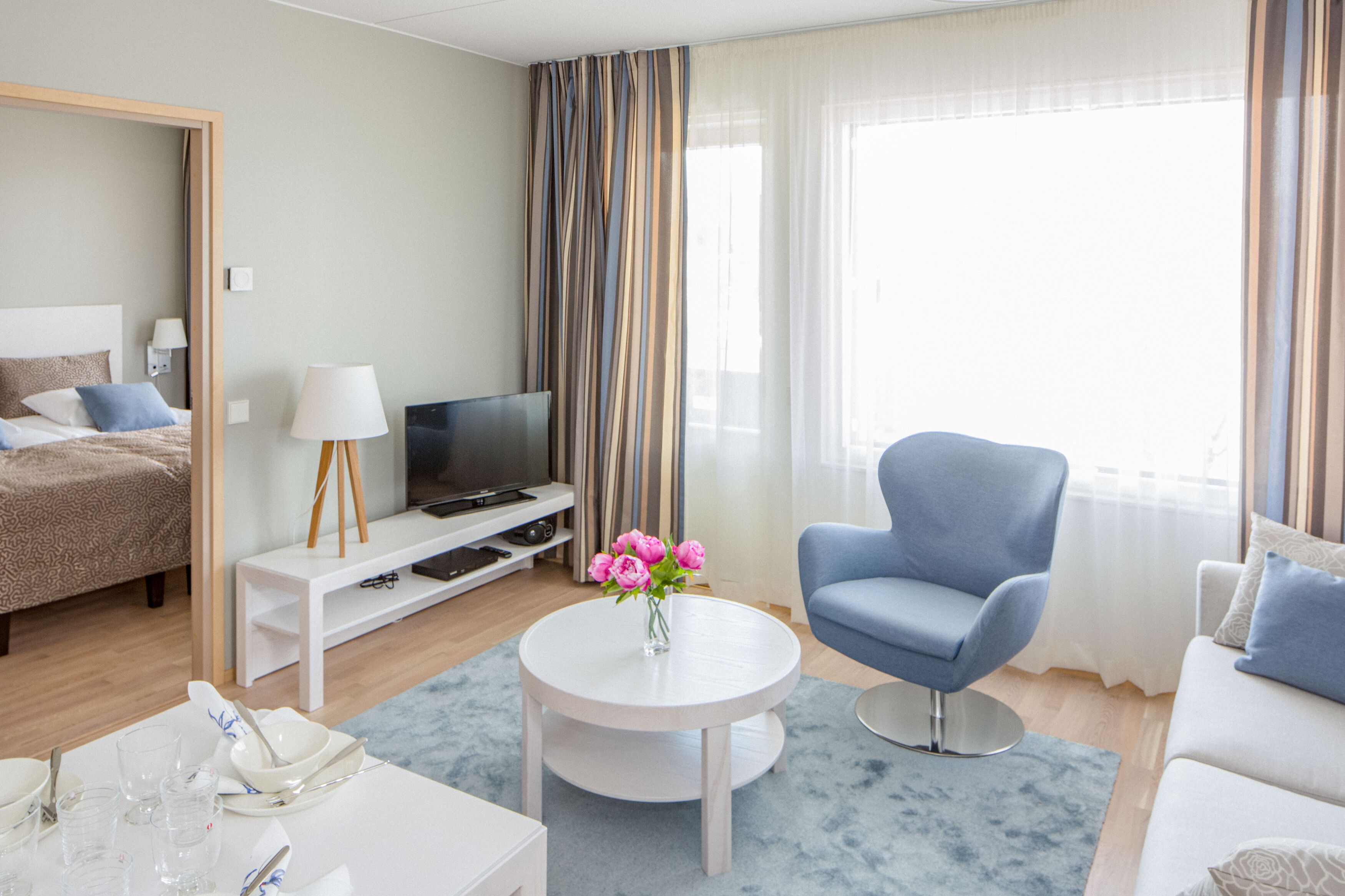 Moderni hotellihuone, jossa on sänky, televisio, oleskelualue ja ruokailutila.