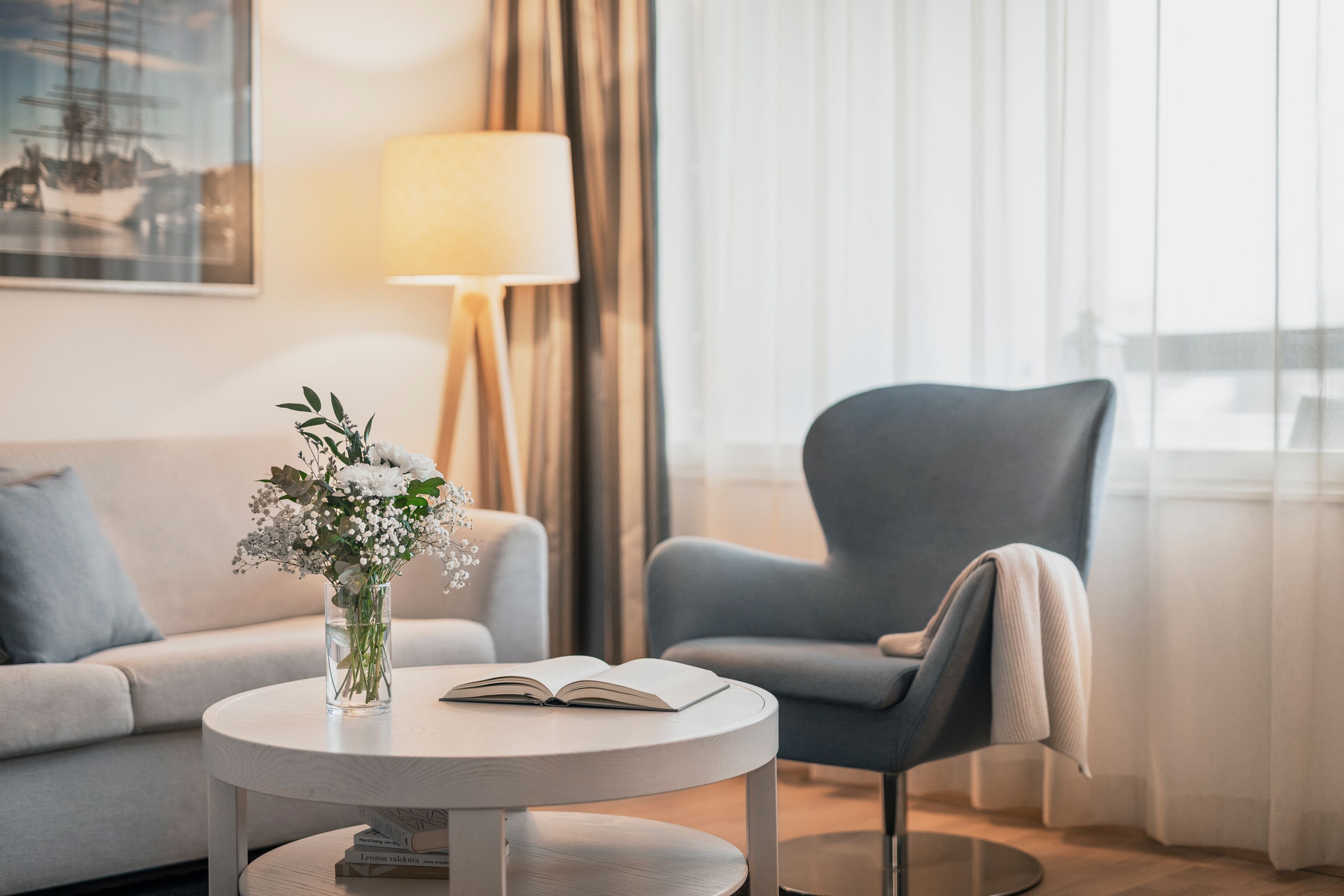 Un salon moderne avec une table ronde, un canapé, un fauteuil bleu, un vase de fleurs et une lampe.