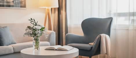 Un salon moderne avec une table ronde, un canapé, un fauteuil bleu, un vase de fleurs et une lampe.