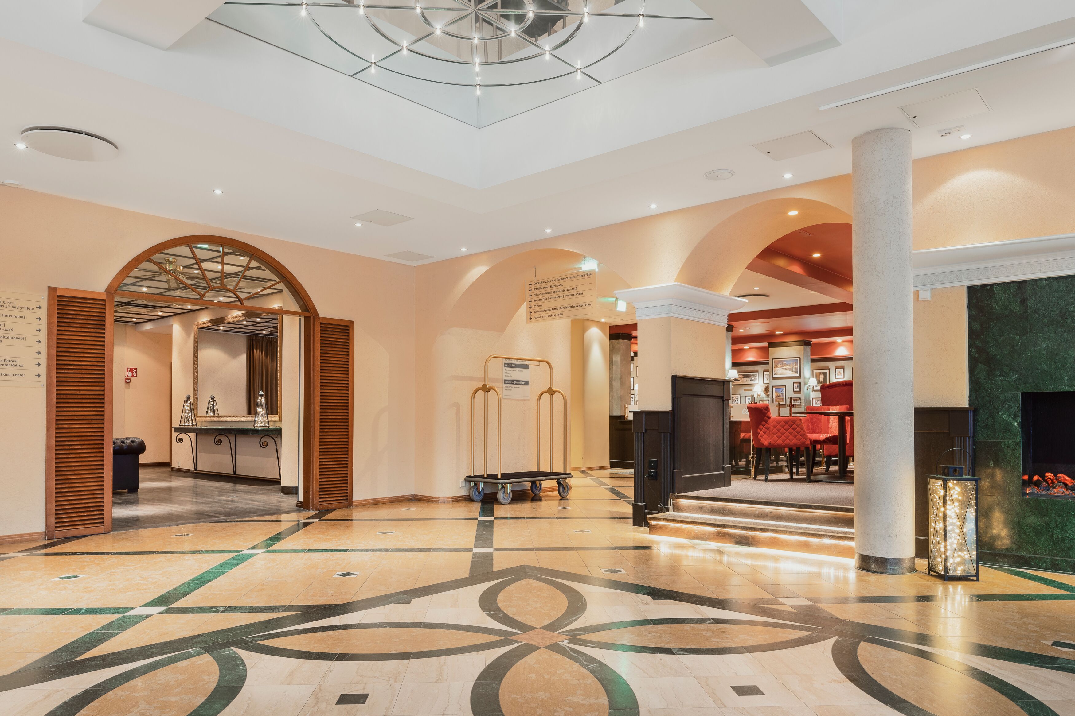 A spacious lobby with a geometric floor pattern, a reception area with a counter and chairs, and a seating area with a fireplace.
