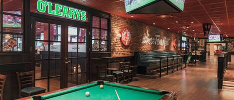 A billiards table with a pool cue and balls, a brick wall with a Boston Red Sox sign, and a bar area with seating.