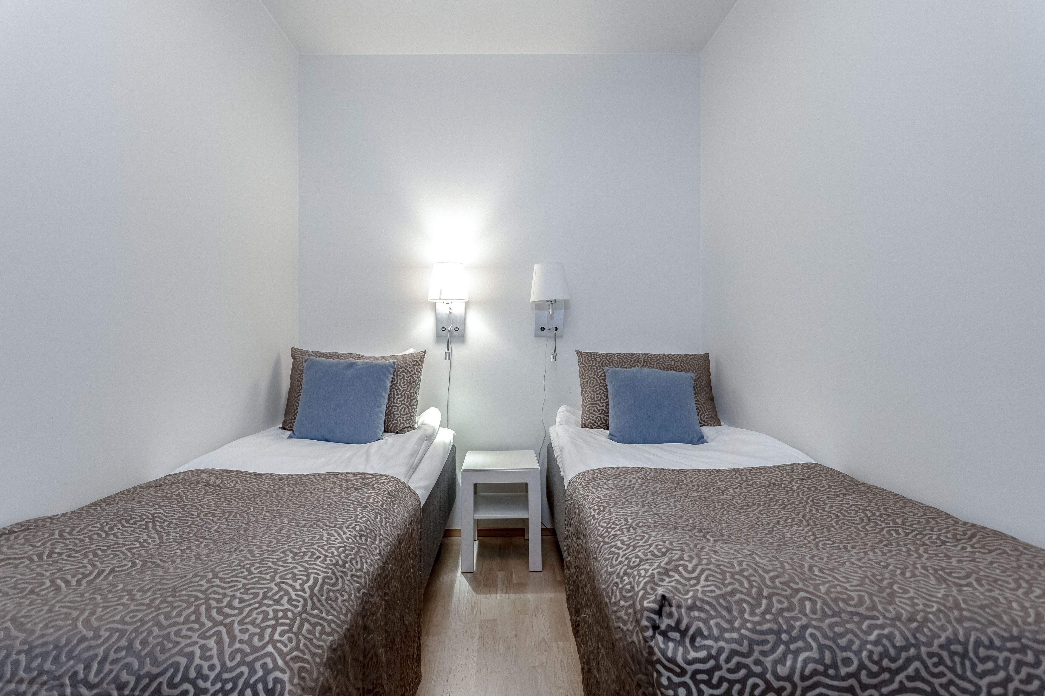 A small, clean room with two beds, a nightstand, and a wall-mounted lamp.