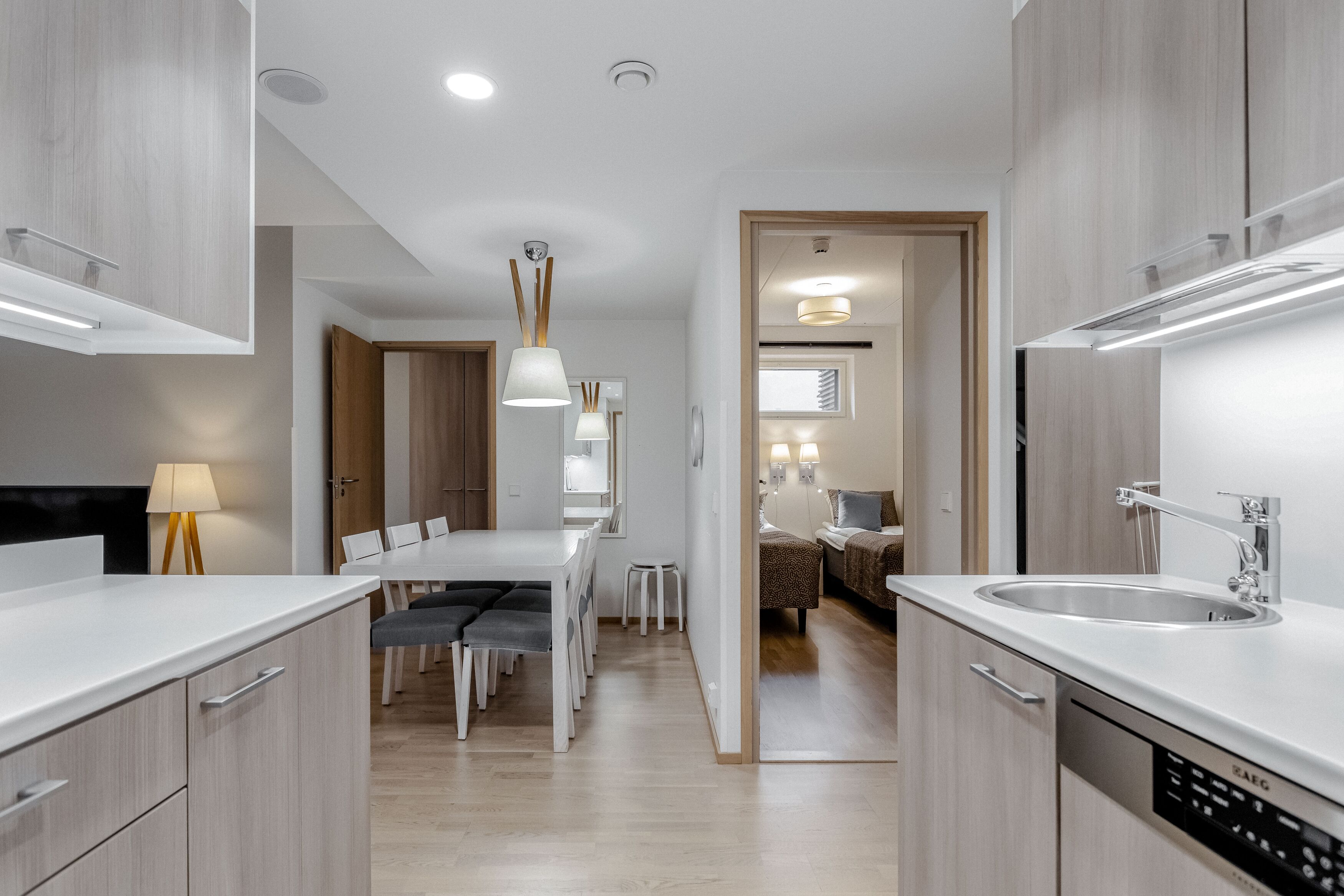A modern kitchen with white cabinetry, a built-in dishwasher, and a dining area with a white table and chairs.