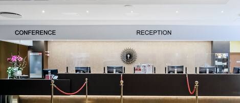 Zona de recepción de un hotel con mostrador, área de conferencias y cartel de recepción.