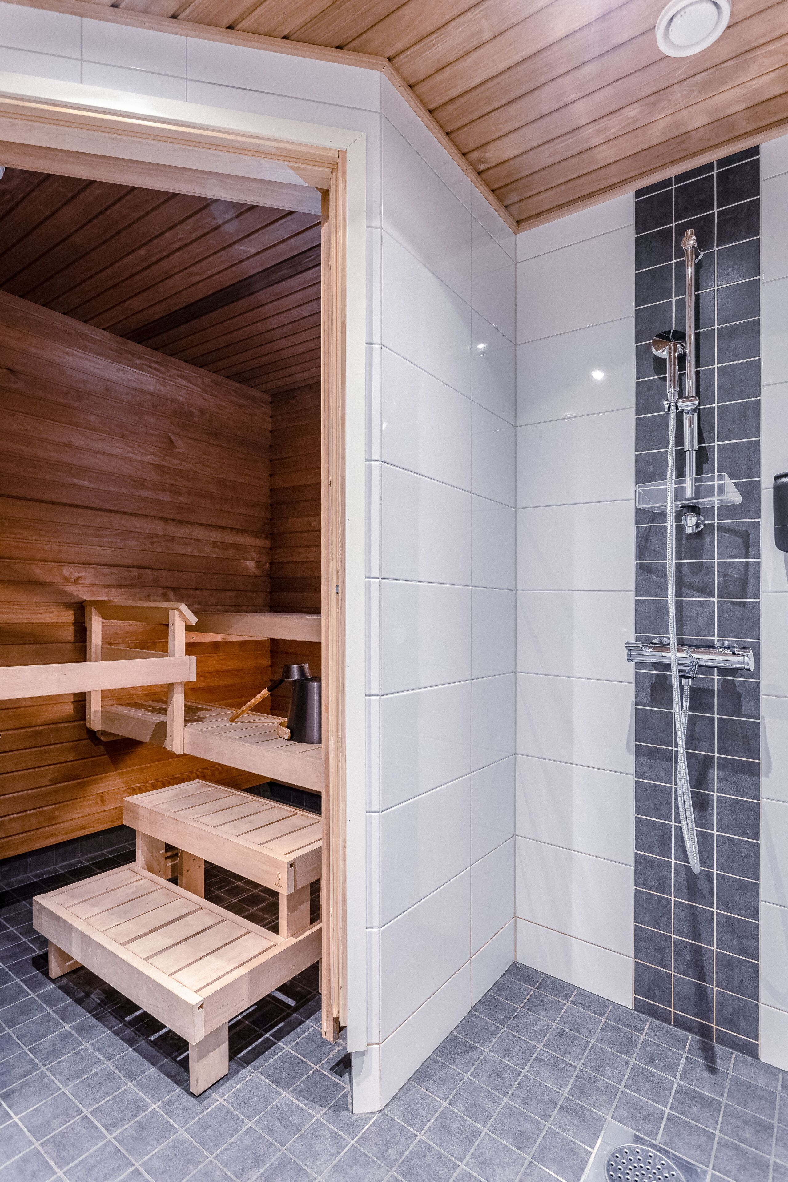 A modern bathroom with a wooden sauna, a shower with a black tiled wall, and a small wooden bench.