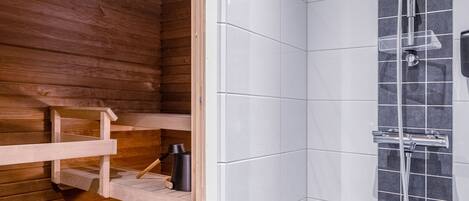 A modern bathroom with a wooden sauna, a shower with a black tiled wall, and a small wooden bench.