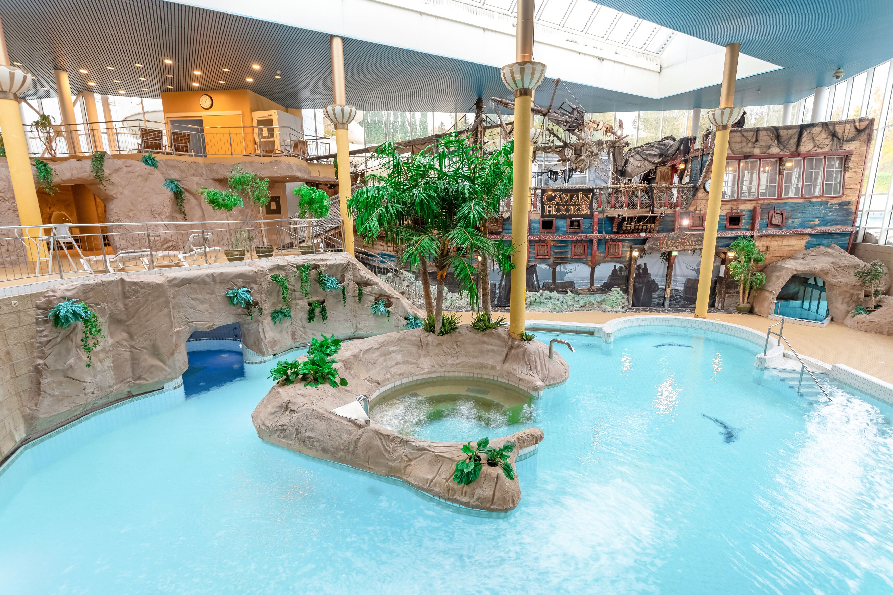 An indoor swimming pool with a tropical theme, including rock formations and plants.