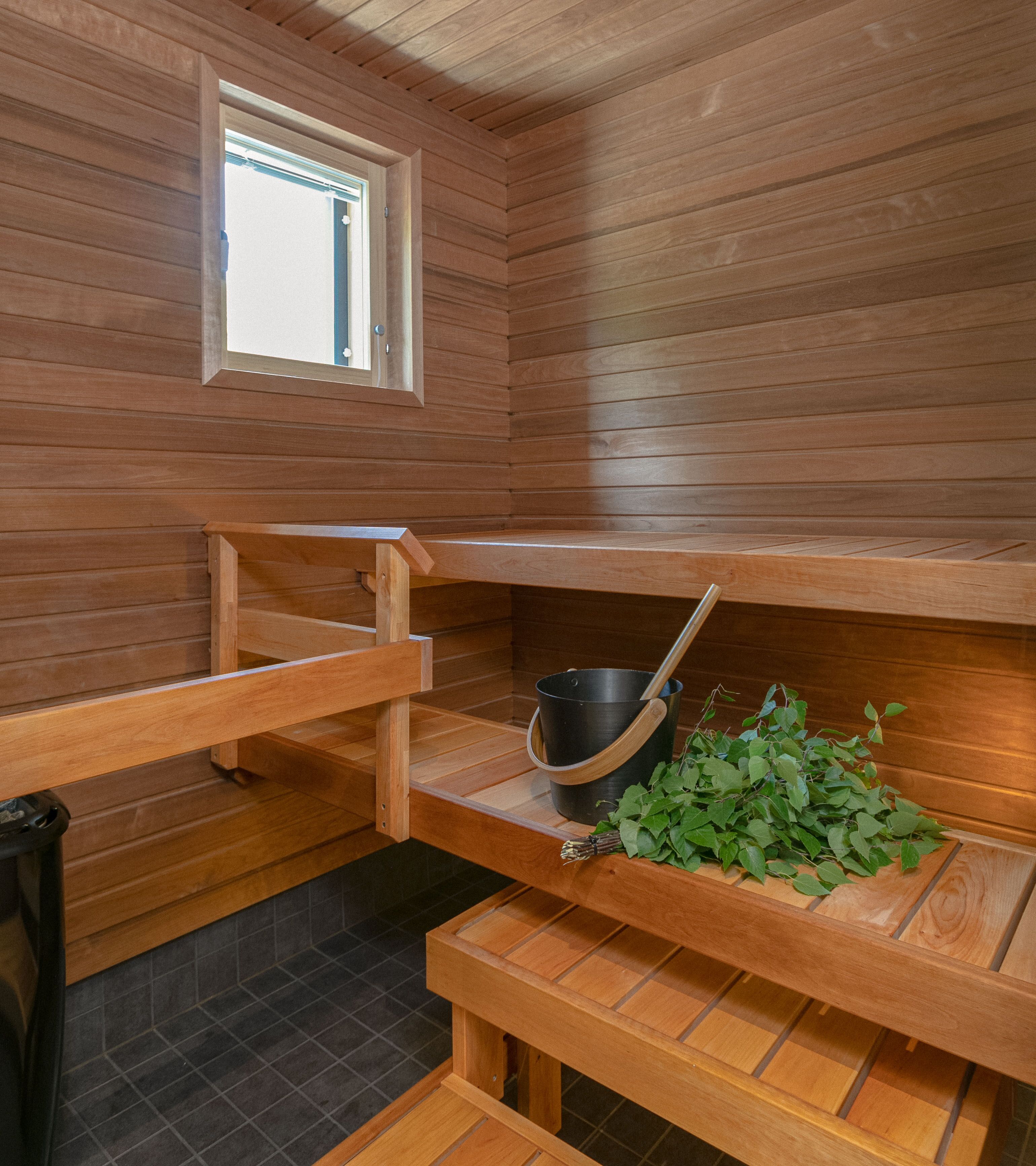 Una sauna con bancos de madera, una ventana y un balde con cuchara de madera.
