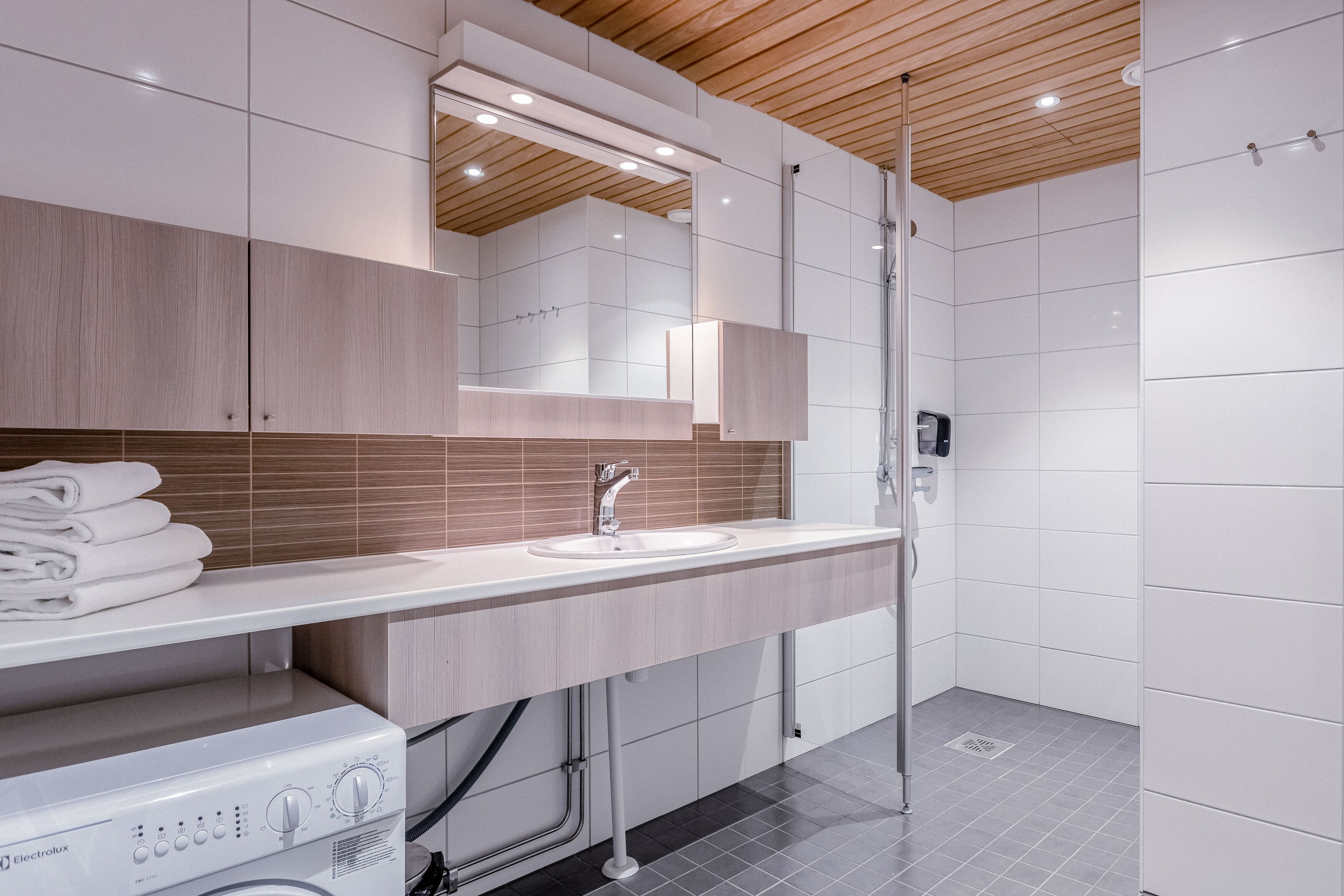 A modern bathroom with a built-in washing machine, a sink, and a shower area.