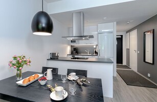 Una cocina moderna con armarios blancos, una campana extractora de acero inoxidable y una lámpara colgante negra.