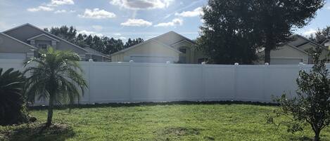 A grassy yard with a white fence, a palm tree, and a large tree.