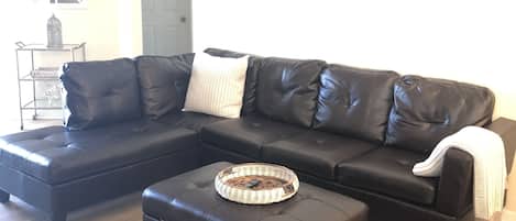 A modern living room with a black leather sectional sofa, a round coffee table, and a shaggy rug.