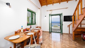A dining area with a wooden table, chairs, and a view of the sea through an open door. - Villa Anastasia - Three Bedroom Villa, Sleeps 6 (Paxi)