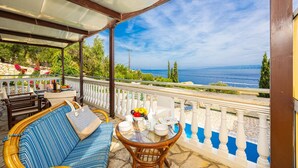 A covered outdoor seating area with a view of the sea, a table with fruits and cups, and a striped sofa. - Villa Anastasia - Three Bedroom Villa, Sleeps 6 (Paxi)