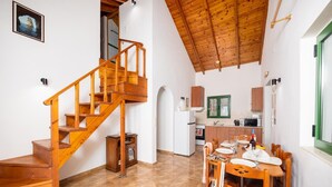 A spacious living area with a wooden staircase, a dining table set for four, and a kitchen in the background. - Villa Anastasia - Three Bedroom Villa, Sleeps 6 (Paxi)