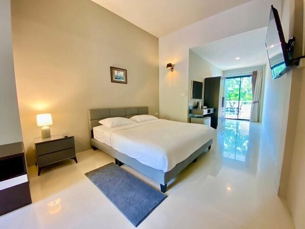 A modern bedroom with a bed, bedside tables, a lamp, a flat-screen TV mounted on the wall, and a large window. - The Green Plaza Hotel (Koh Samui)