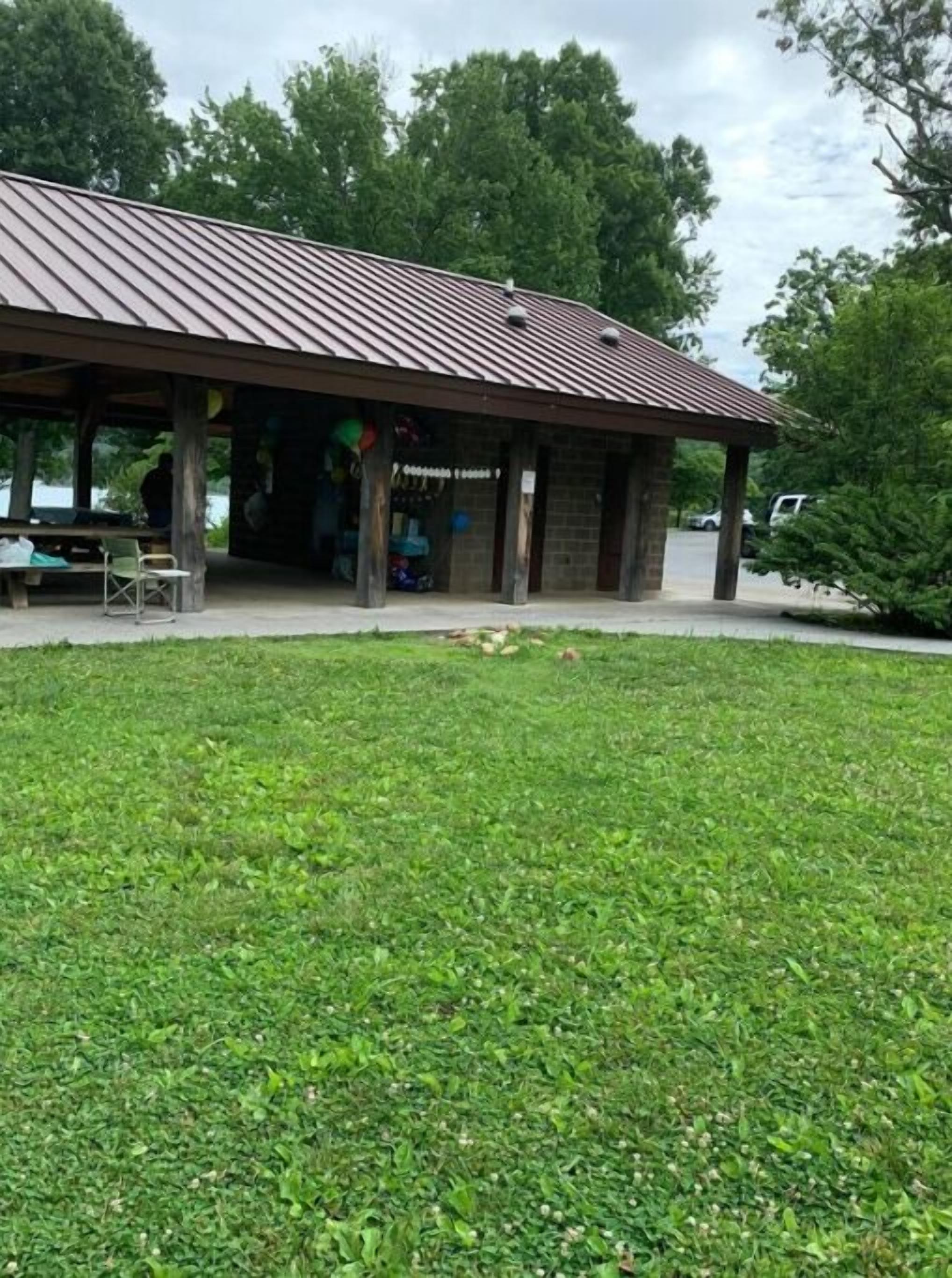 Un pavillon couvert, à l’extérieur en briques et doté d’un toit en métal, entouré d’une zone herbeuse.