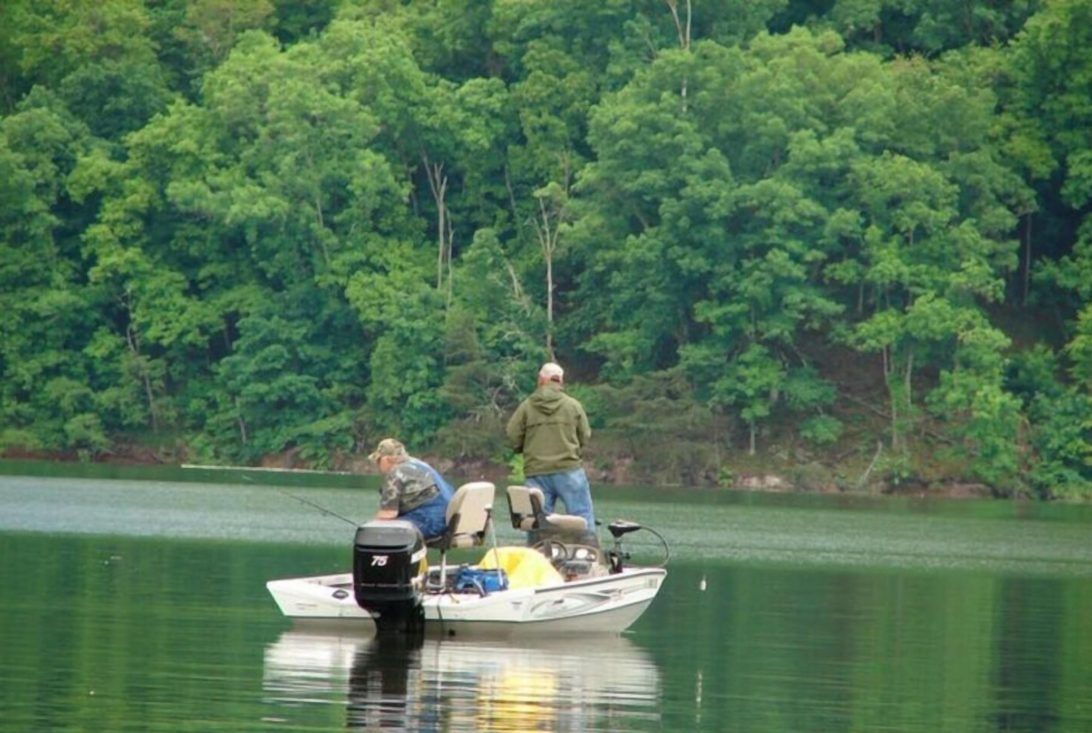 Un bote en un lago tranquilo con dos personas pescando, rodeado de árboles verdes y frondosos.