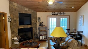 A cozy living room with a stone fireplace, a ceiling fan, a sofa, and a dining area with a table and chairs. - Paradise Peak - Tranquility and majestic splendor! (Butler)